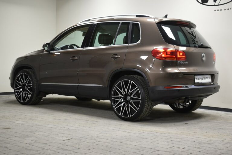 A brown Volkswagen Tiguan is parked indoors, facing a wall. The car has large black and silver wheels and tinted windows.