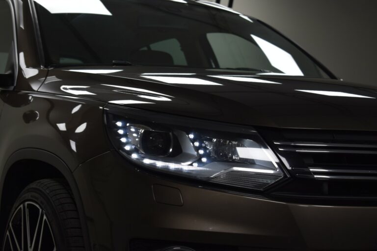 Close-up of a brown SUV's front showing the headlight and part of the grille under bright lighting.