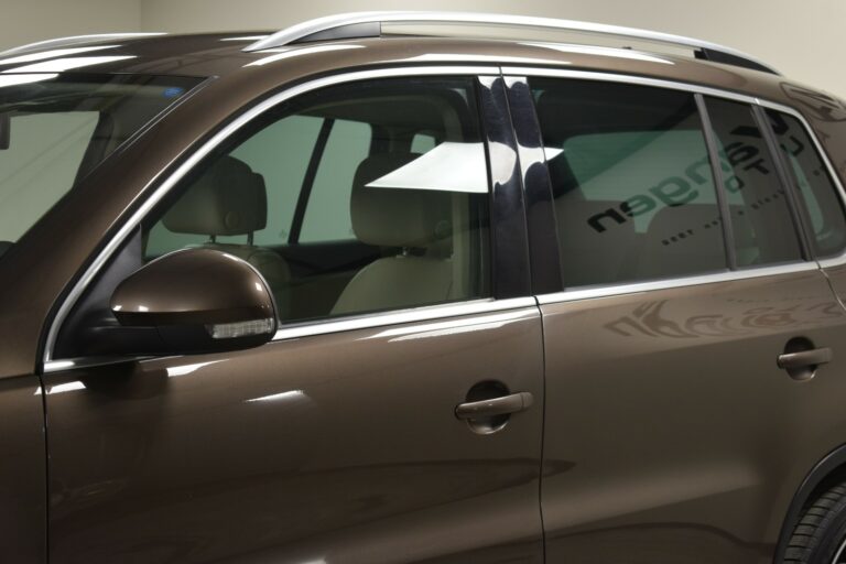 A brown SUV is parked indoors with a view of the side mirror, windows, and roof rails.