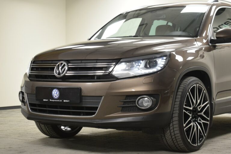 Close-up of a brown Volkswagen SUV showcasing its front grille, headlights, and alloy wheel on a textured floor.