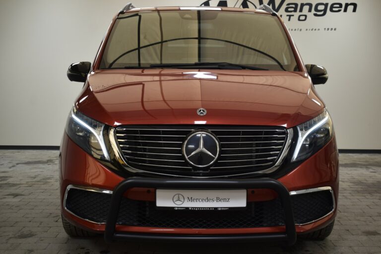 Front view of a red Mercedes-Benz van with a prominent grille and Mercedes logo. The background features a logo and text on a wall.