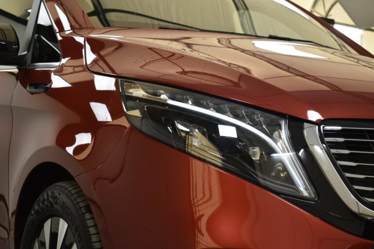 Close-up of a shiny red car's front headlight and grille, showing reflections and detailing.