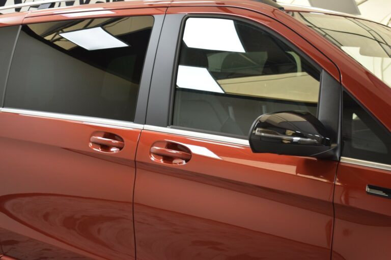 A close-up of a red vehicle's side, showing tinted windows, side mirror, and door handles.