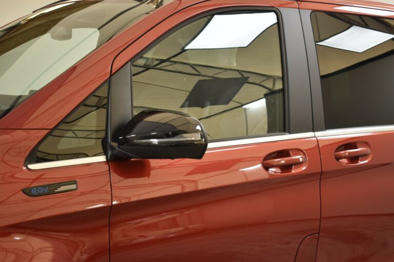 Close-up of a red vehicle's side, showing the door, side mirror, and window.