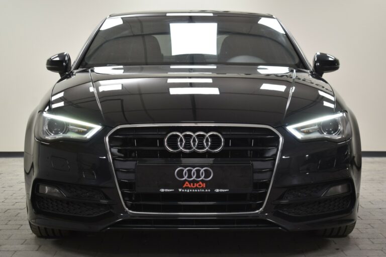 Front view of a black Audi car with LED headlights, parked on a tiled floor, displaying the Audi logo and grille.