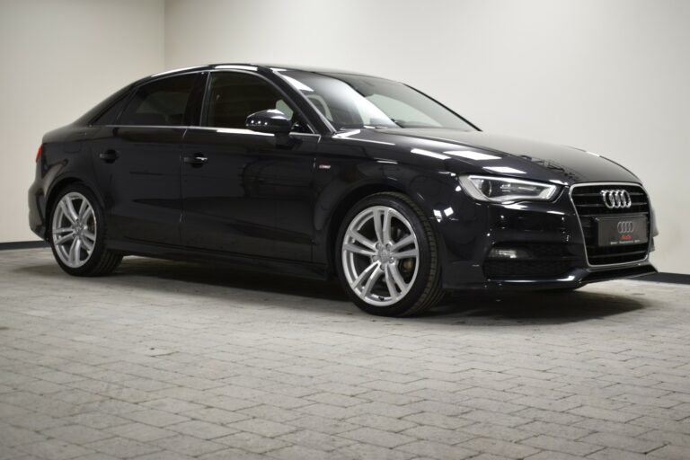 A black Audi sedan parked in a well-lit indoor space on a paved surface.