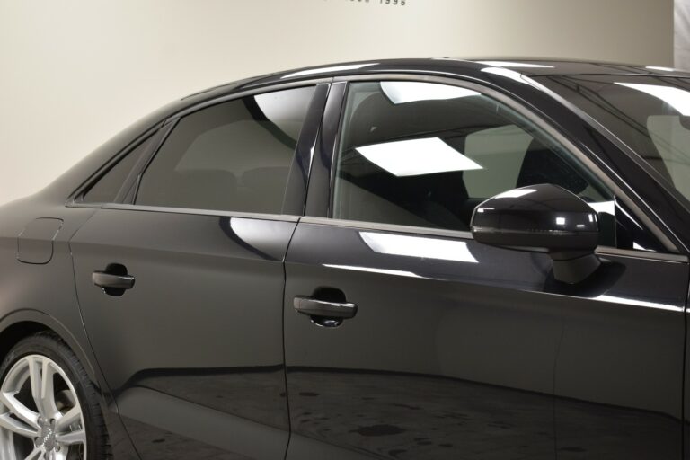 Side view of a black car showing the rear door, window, and side mirror with a reflection of ceiling lights.