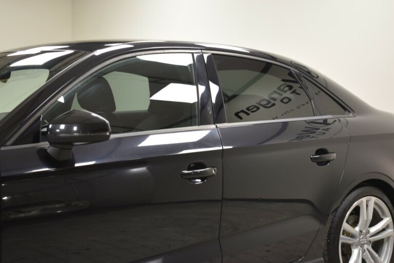 Side view of a black sedan car in a showroom with reflective windows and silver wheel rims.