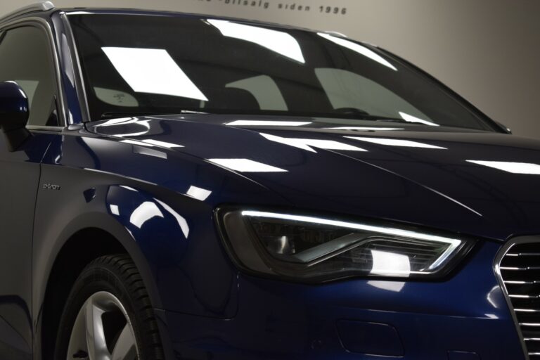 Close-up of the front section of a dark blue car, focusing on the headlight and a portion of the hood.