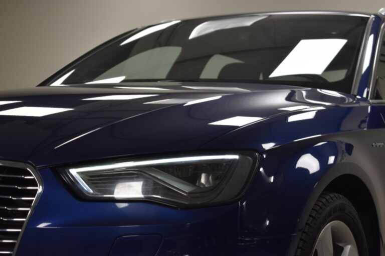 Close-up of the front left side of a blue car, focusing on the headlight and part of the hood.