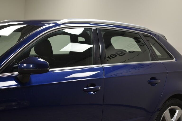 Side view of a blue car with tinted windows, silver roof rails, and a visible side mirror in a well-lit indoor setting.