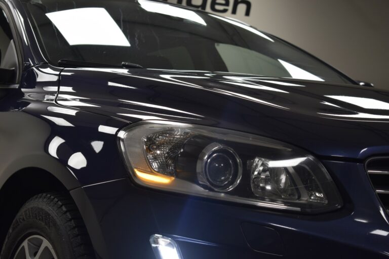 Close-up of a dark blue car's front with headlights on, reflecting overhead lights on the glossy surface.