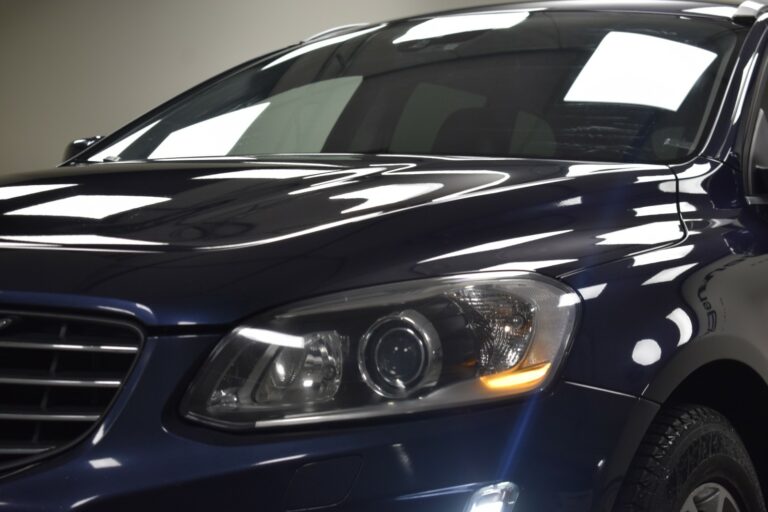 Close-up of a dark blue car's front showcasing the headlight, grille, and part of the hood with reflective lighting.