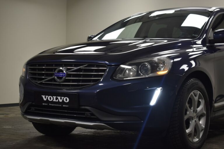 Close-up of a dark blue Volvo SUV from the front side, showing the grille, headlights, and part of the wheel, parked indoors.