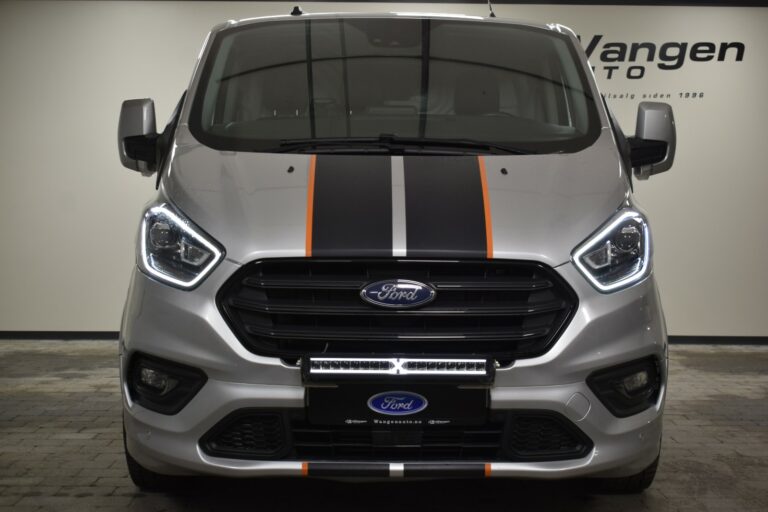 Front view of a Ford van with a silver body, black and orange racing stripes, and LED headlights in an indoor setting.