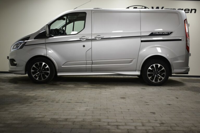 A silver Ford Transit van is parked indoors, viewed from the side, with black and silver wheels and "Transit" logo visible.