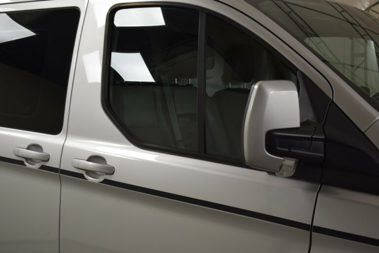 Close-up of the driver's side of a white van, showing the side mirror and part of the door with tinted windows.