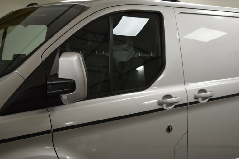 A white van with tinted windows and a black stripe on the side, viewed from the front left angle in an indoor setting.