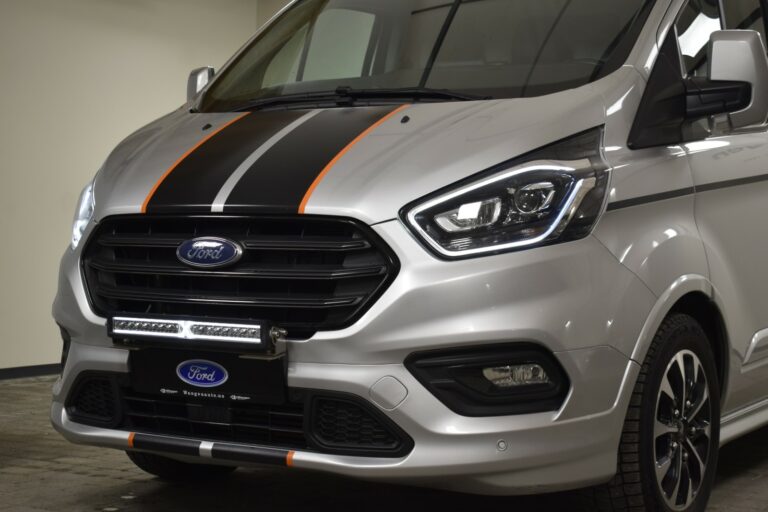 Front view of a silver Ford van with black and orange stripes on the hood and a Ford logo on the grille.