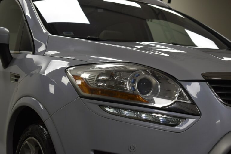 Close-up of a silver SUV's front headlight and surrounding area, showing reflective surfaces and sleek design details.