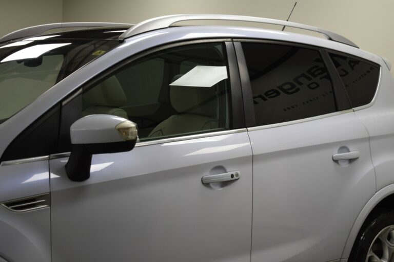 Side view of a silver SUV with tinted windows, parked indoors, showing the rear-view mirror and roof rails.